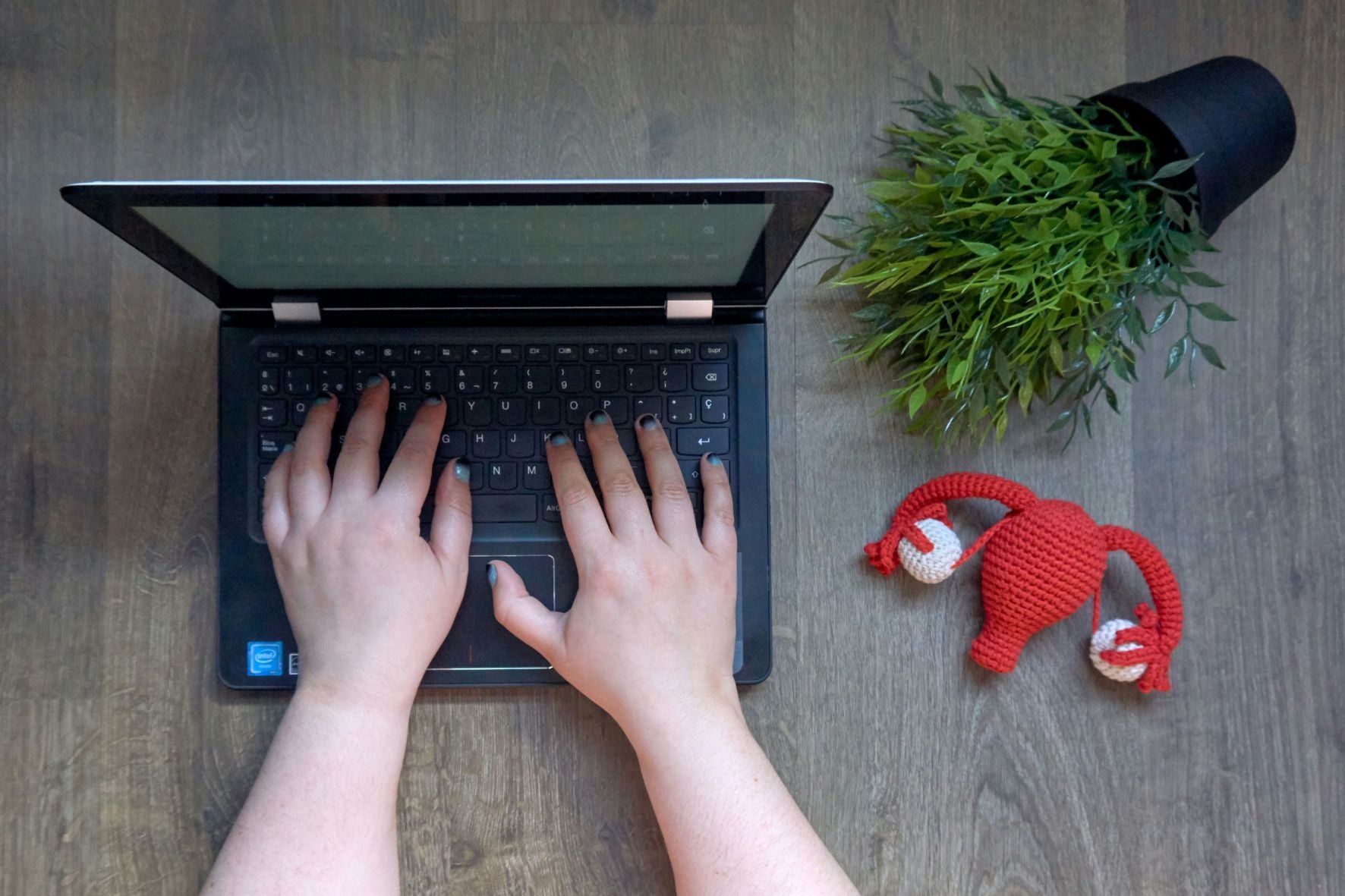 Deux mains au-dessus d’un clavier d’ordinateur portable avec un utérus au crochet déposé à côté.